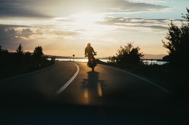 Človek v stoji šoféruje motorku pri západe slnka